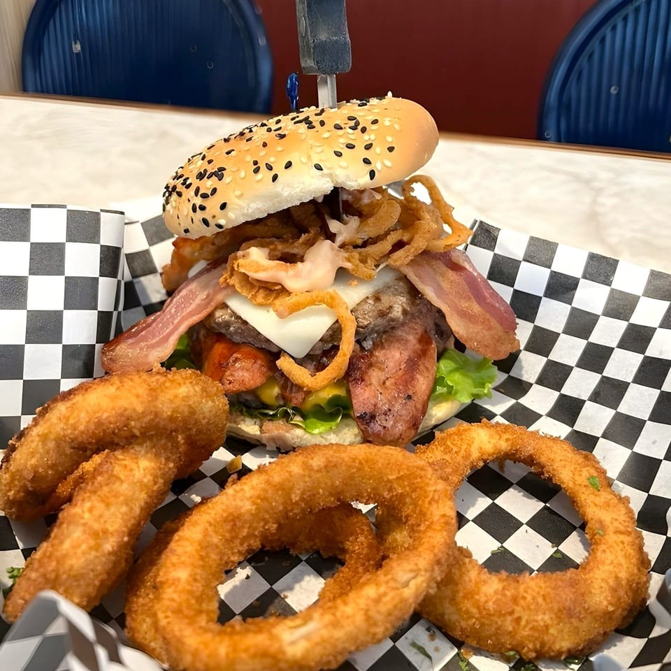 A Woody's Classic Grill burger with bacon, onion rings, and cheese, served with a side of onion rings.