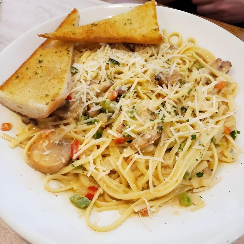 Creamy pasta with mushrooms, bell peppers, and grated cheese, served with two pieces of garlic bread.