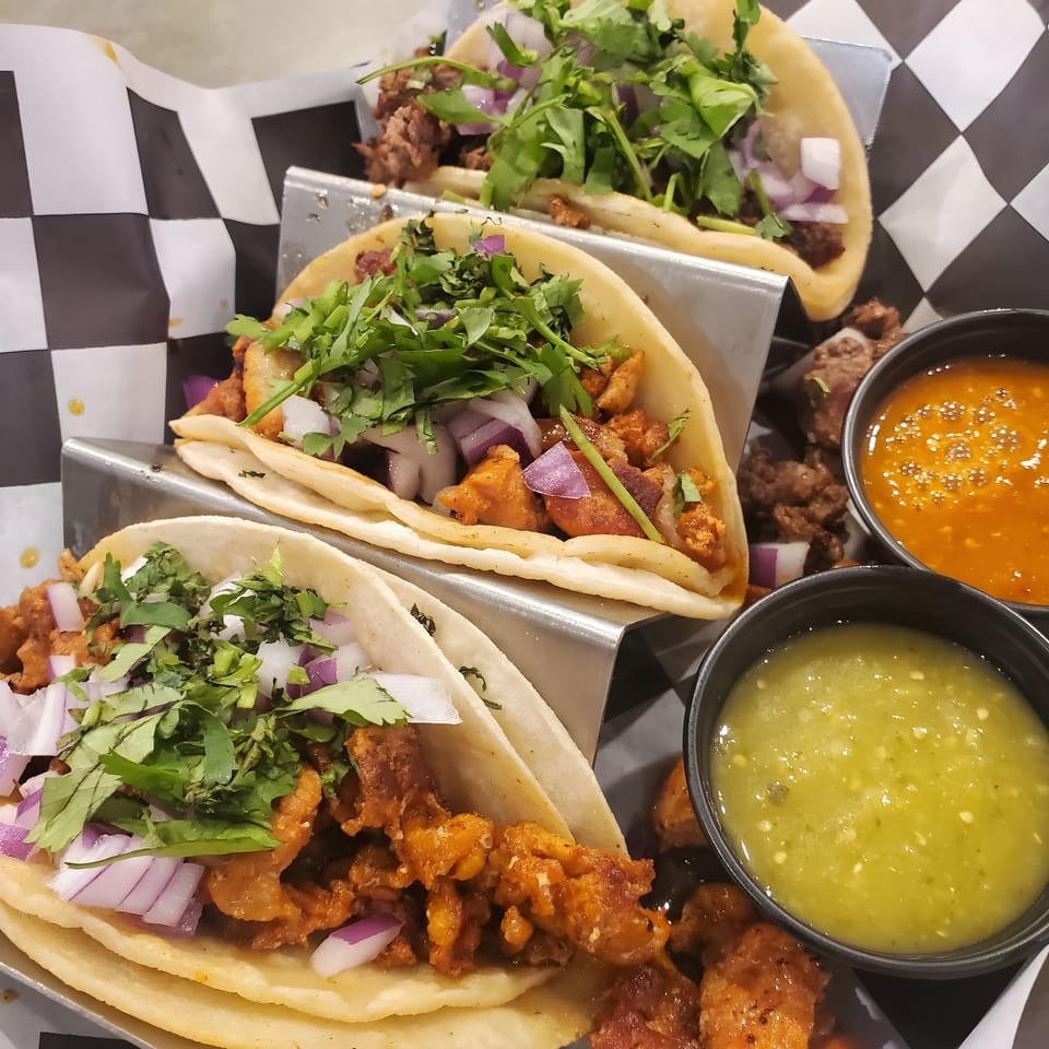 Three tacos with meat, cilantro, and red onion, served with red and green salsa.