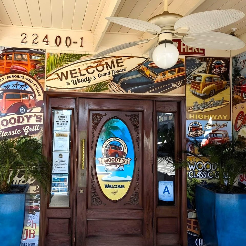 Woody's Classic Grill entrance with a wooden door, vintage car murals, and a "Welcome" sign.