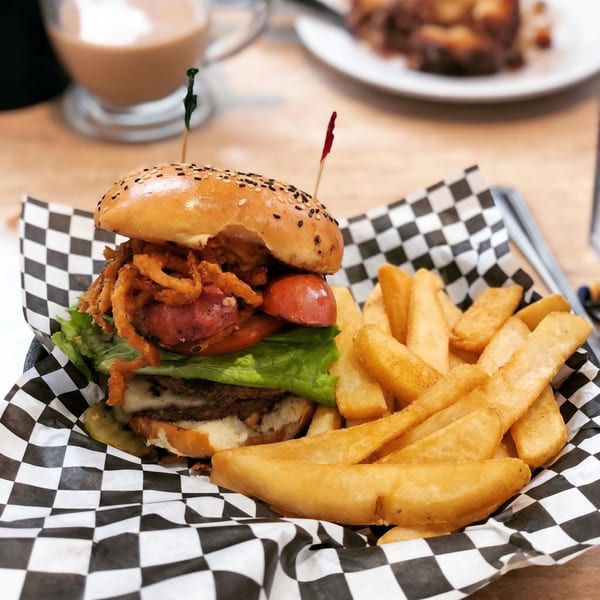 A loaded burger with onion rings, lettuce, tomato, and fries in a checkered basket.
