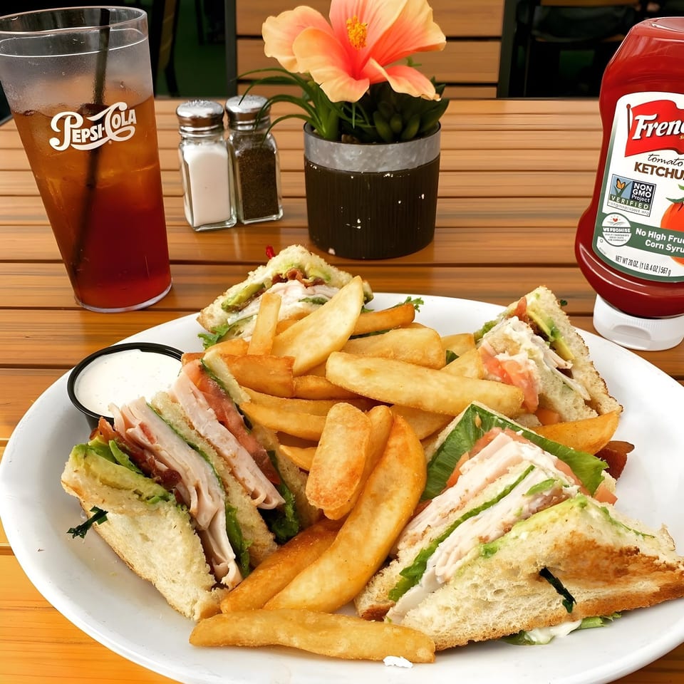 A Woody's Classic Grill club sandwich with fries, ranch, Pepsi, and ketchup on a wooden table.