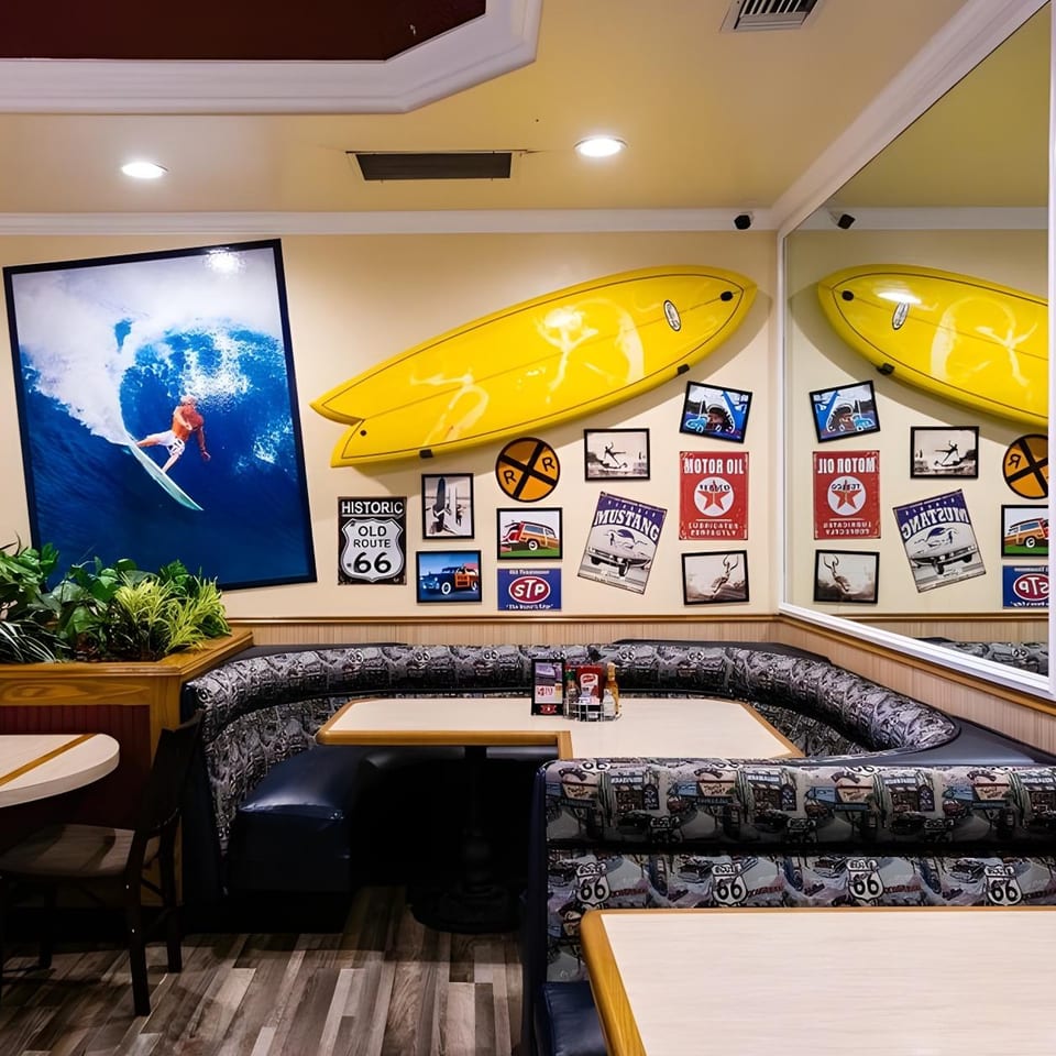 Diner interior with Route 66 themed booths, a large surfing print, and yellow surfboards on the wall.