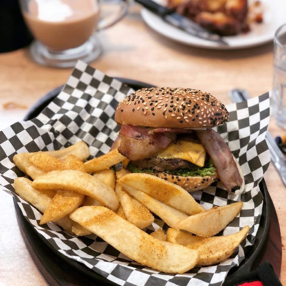 A bacon cheeseburger with sesame seed bun and a side of seasoned potato wedges in a black basket.